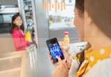 A mother checking the temperature and contents of her fridge from her phone as her daughter puts groceries away.